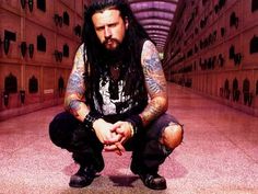 a man with long hair and piercings crouching down in an alleyway, holding his hands together