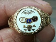 a gold ring with an eye, skull and crossbones on the front is in someone's hand