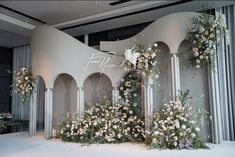 an arrangement of flowers and greenery on display in front of a white wall with columns