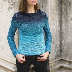 a woman standing in front of a wall with her hands on her hips wearing a blue sweater