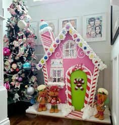 a pink gingerbread house decorated with candy canes and christmas decorations next to a tree