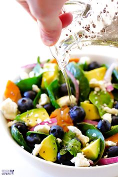 someone is pouring dressing into a salad with blueberries, avocado, and spinach