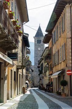 a clock tower is in the distance between two buildings and a cobblestone street