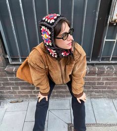 a woman wearing sunglasses and a hat is sitting on the sidewalk with her hands behind her head