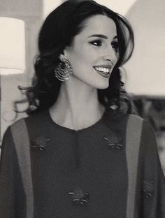 a black and white photo of a woman with long hair smiling at the camera while wearing earrings