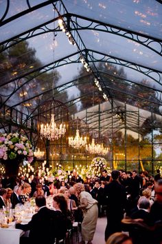 a large group of people sitting at tables in a room with chandeliers hanging from the ceiling