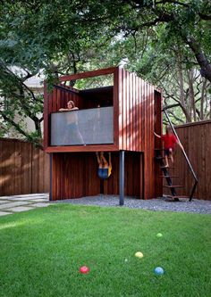 two people climbing up the side of a wooden structure in a yard with balls on the ground