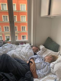 two people laying on a bed in front of a window with windowsills behind them