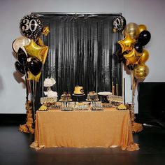 a table topped with balloons and cake next to a black drape curtain covered wall