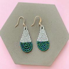 a pair of beaded earrings sitting on top of a hexagonal tile piece