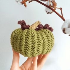 a hand holding up a knitted pumpkin ornament in front of a cotton plant