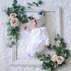 a baby is laying on the floor next to flowers and greenery in a frame