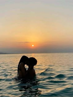 two people kissing in the water at sunset