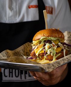 a person holding a tray with a large sandwich on it and a toothpick sticking out of the top