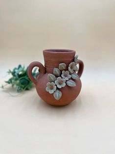 a brown vase with flowers on it sitting next to a plant