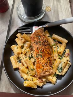 a black plate topped with pasta and meat next to a glass of soda on a table