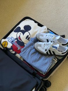 an open suitcase with shoes and clothing in it sitting on the floor next to a piece of luggage