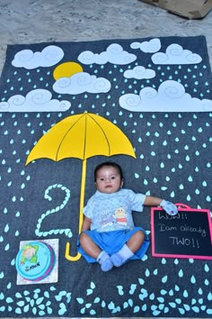 a baby sitting on the ground with an umbrella and chalkboard in front of it