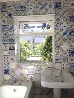 a white sink sitting under a window next to a bath tub in a room with blue and white tiles on the walls