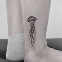 a black and white photo of a jellyfish tattoo on the ankle, with its long tentacles sticking out