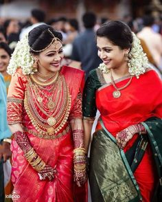 two women in red and green saris smile at each other