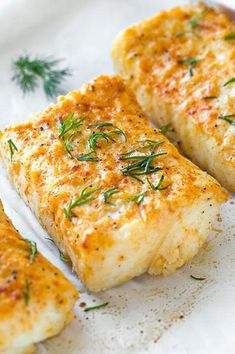 three fish fillets on a white plate with herbs sprinkled on the side