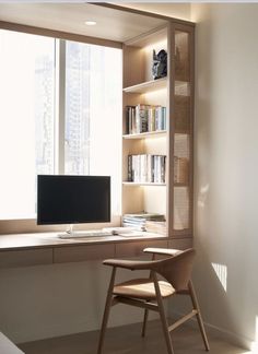 a desk with a computer on it in front of a window and bookshelf