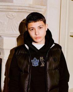 a young man in a black jacket standing next to a fireplace