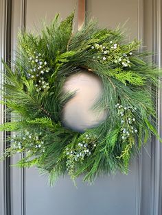 a green wreath with white flowers and greenery hangs on the front door's glass door