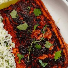 a white plate topped with meat and rice covered in cilantro next to a lemon wedge