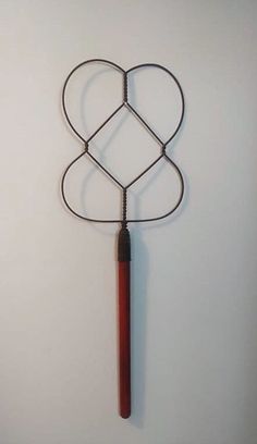 a heart shaped metal object hanging on the wall next to a wooden stick with a handle