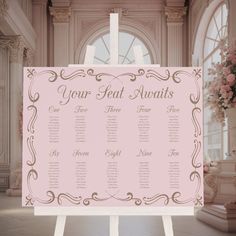 a pink wedding seating chart on a white easel in front of a large window