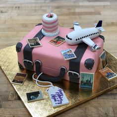 a cake shaped like a pink suitcase with an airplane on top and pictures around it