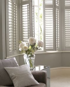 a living room with white shutters and flowers in a vase