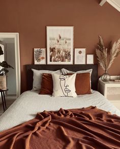 a bed with orange and white pillows in a bedroom next to pictures on the wall