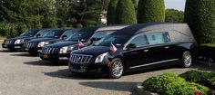 a row of black limos parked in front of trees and bushes with an american flag on the roof