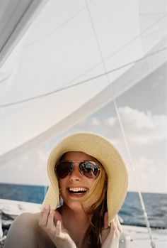 a woman in a yellow hat and sunglasses on a boat with the ocean behind her