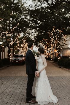 a bride and groom are standing in front of some trees with lights on them at night