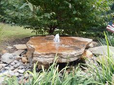 there is a rock fountain in the middle of some grass and rocks, with an american flag in the background