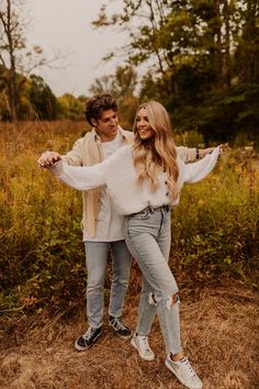 a man and woman are posing for a photo in front of some tall grass with their arms around each other