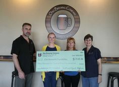 three people holding a large check in front of a wall with a logo on it