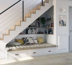 there is a bench under the stairs in this room with bookshelves and pillows