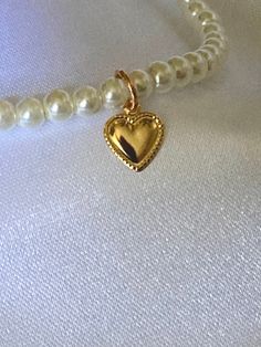 This necklace has 4mm round glass pearls. The necklace is accented with a gold heart charm. Gold Pearl Jewelry With Heart Charm, Gold Pearl Necklace With Heart Pendant And Beads, Gold Pearl Necklace With Heart Charm And Pendant, Vintage Gold Charm Necklace With Pearl, Gold Charm Necklace With Pearl Charm And Round Beads, Vintage Gold Necklace With Pearl Charm, Dainty Gold Pearl Necklace With Heart Pendant, Dainty Gold Heart-shaped Pearl Necklace, Gold Heart-shaped Pearl Pendant Necklace