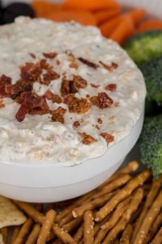 a bowl of dip surrounded by crackers, broccoli and carrots