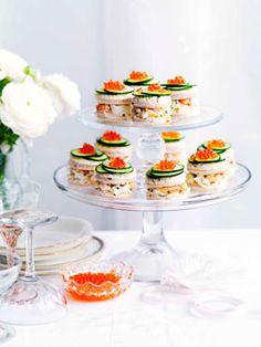 there are many small sandwiches on the trays next to some glasses and flowers in vases