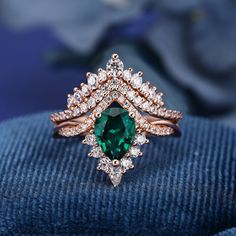 an emerald and diamond ring sitting on top of a blue cloth