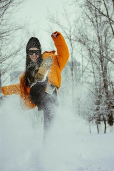 a person in an orange jacket is snowboarding down a hill with trees behind them