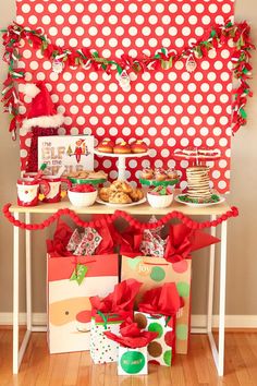 a table topped with lots of presents under a red polka dot wall and christmas decorations