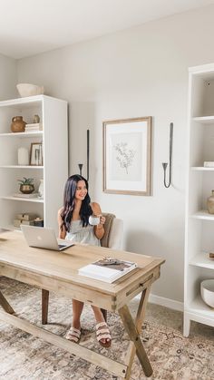 a woman sitting at a table with a laptop on her lap and holding a cup