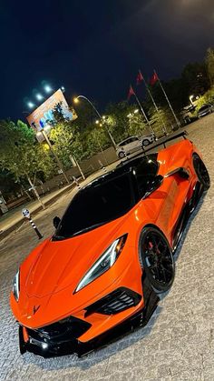 an orange sports car parked in front of a tall building at night with its lights on